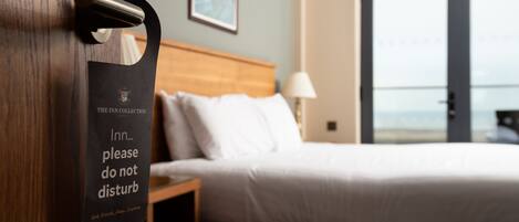 A hotel room with a bed, a nightstand, a lamp, and a door with a sign.