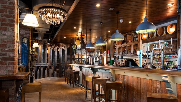 A bar area with wooden bar stools, hanging pendant lights, and a brick wall. - The Commissioners Quay Inn - The Inn Collection Group (Blyth)