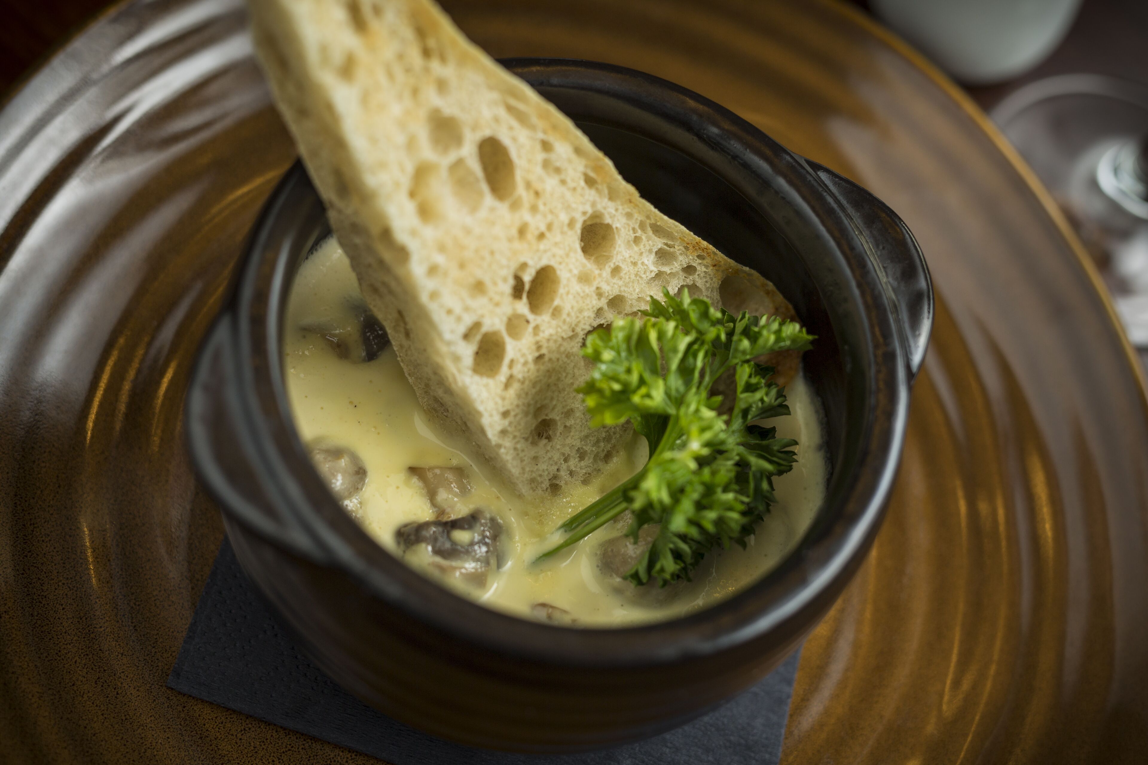 A bowl of soup with bread and parsley on a plate.