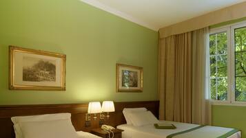 Quarto de hotel com duas camas, uma mesa de cabeceira com telefone, duas luminárias na parede e duas imagens emolduradas.