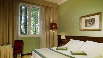A hotel room with a bed, a table with a plate of fruit, a chair, a lamp, and a framed picture on the wall.