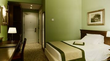 A hotel room with a bed, a desk, and a chair. There is a door leading to another room.