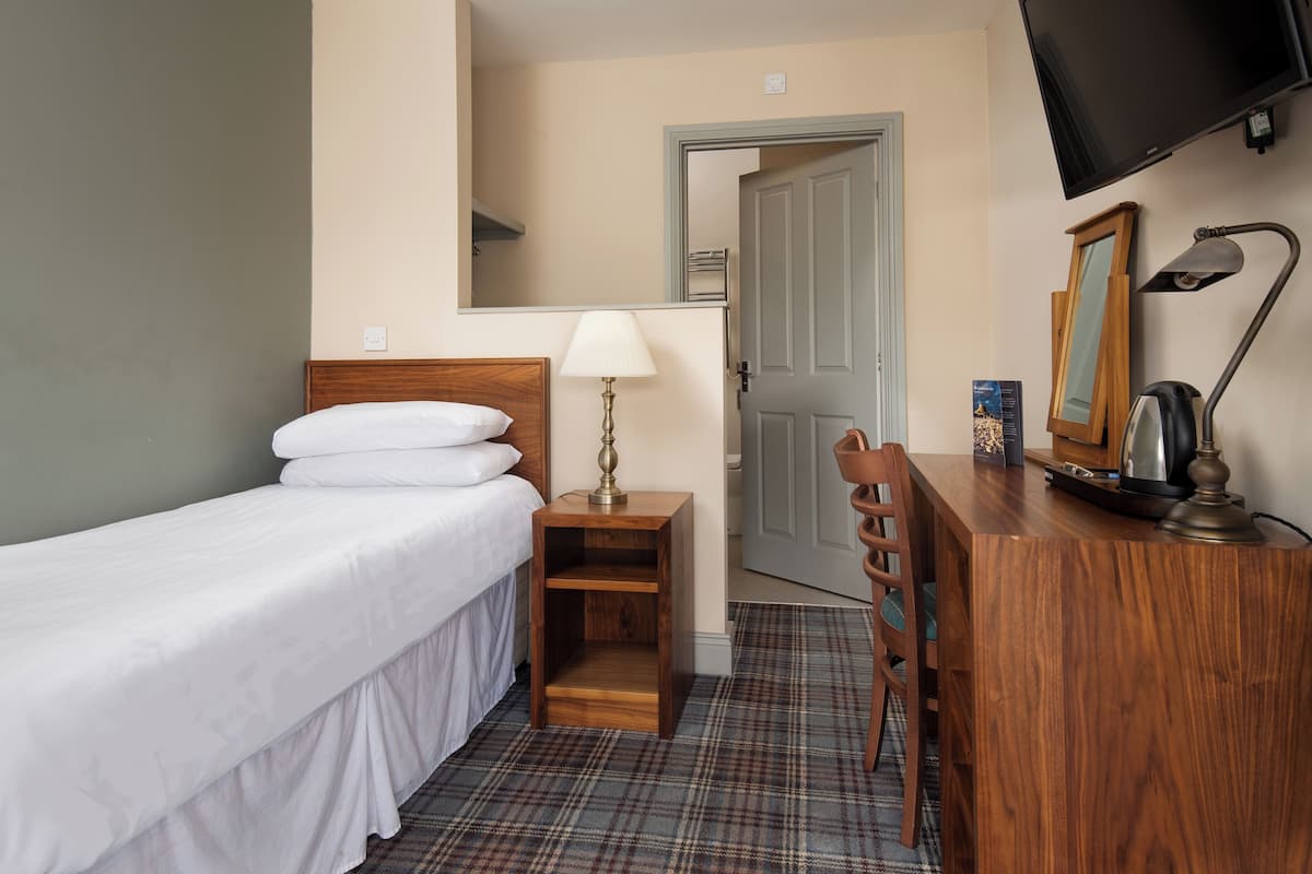 Une chambre d’hôtel comprenant un lit, une table de chevet avec une lampe, une commode, un miroir et un téléviseur.