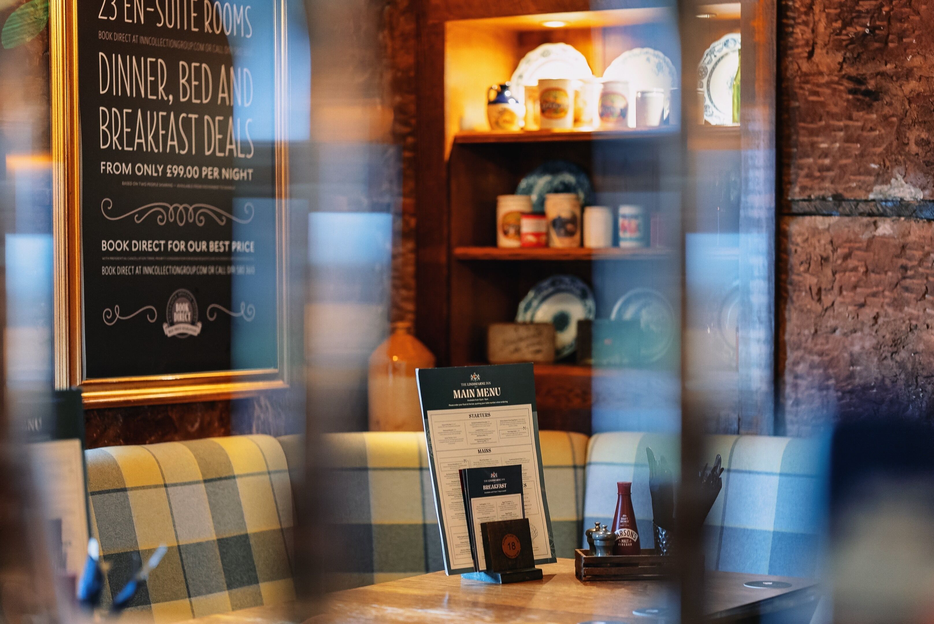 A menu board with room rates and breakfast deals, a checkered sofa, and a shelf with dishes.