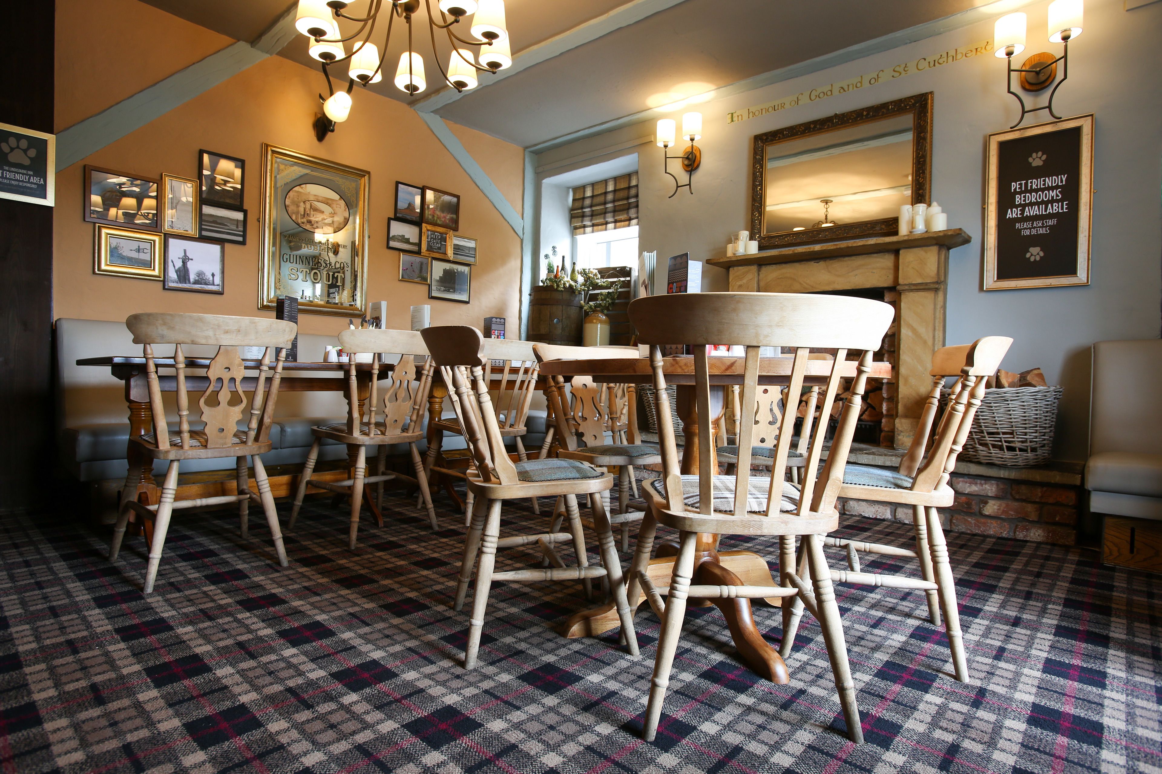 A cozy dining area with wooden chairs and a checkered floor, featuring a fireplace and framed pictures on the walls.