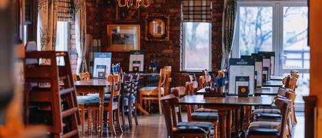 A restaurant with wooden tables and chairs, a brick wall, and a chandelier.