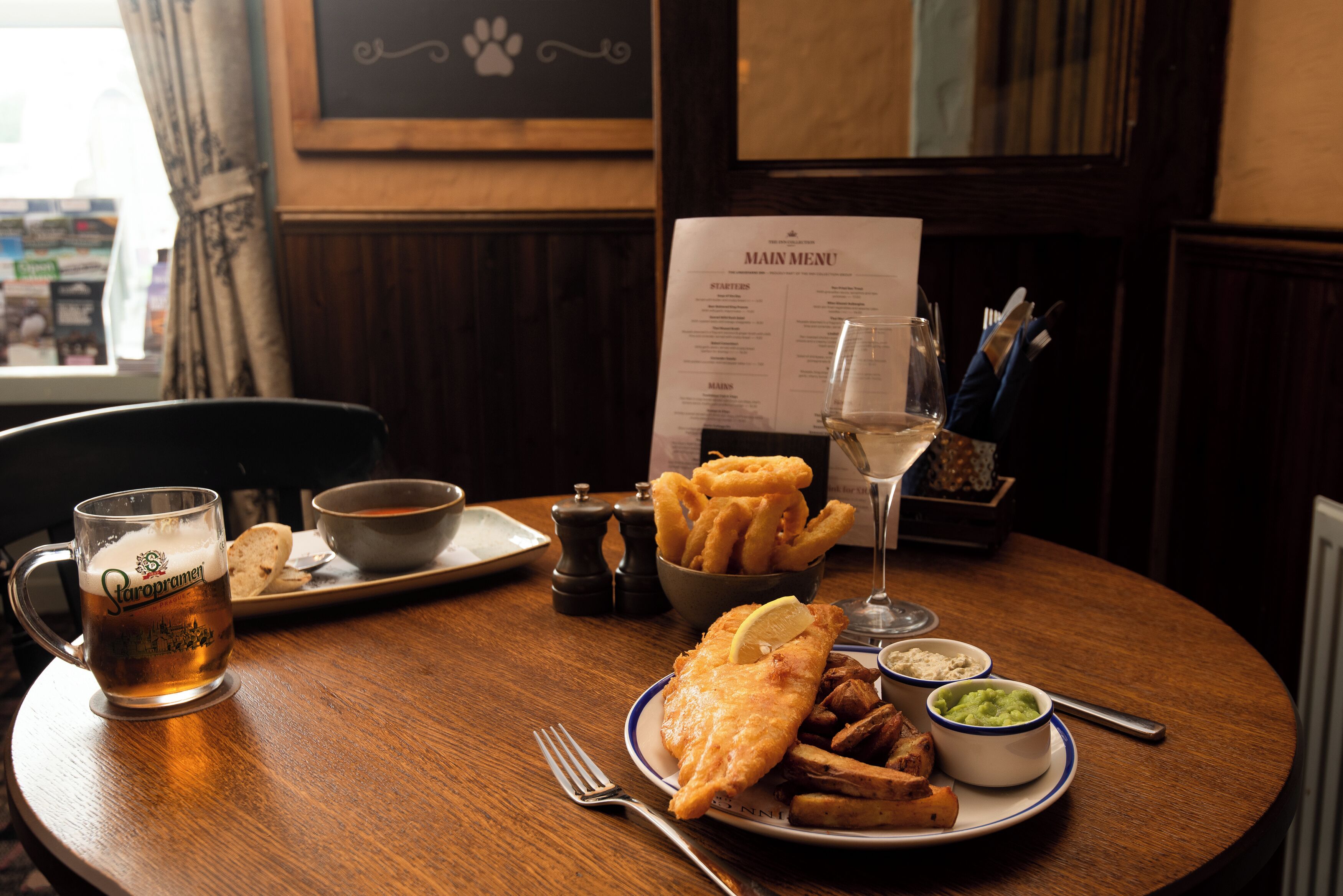 A table with a meal consisting of fish and chips, a glass of beer, and a bowl of mush.