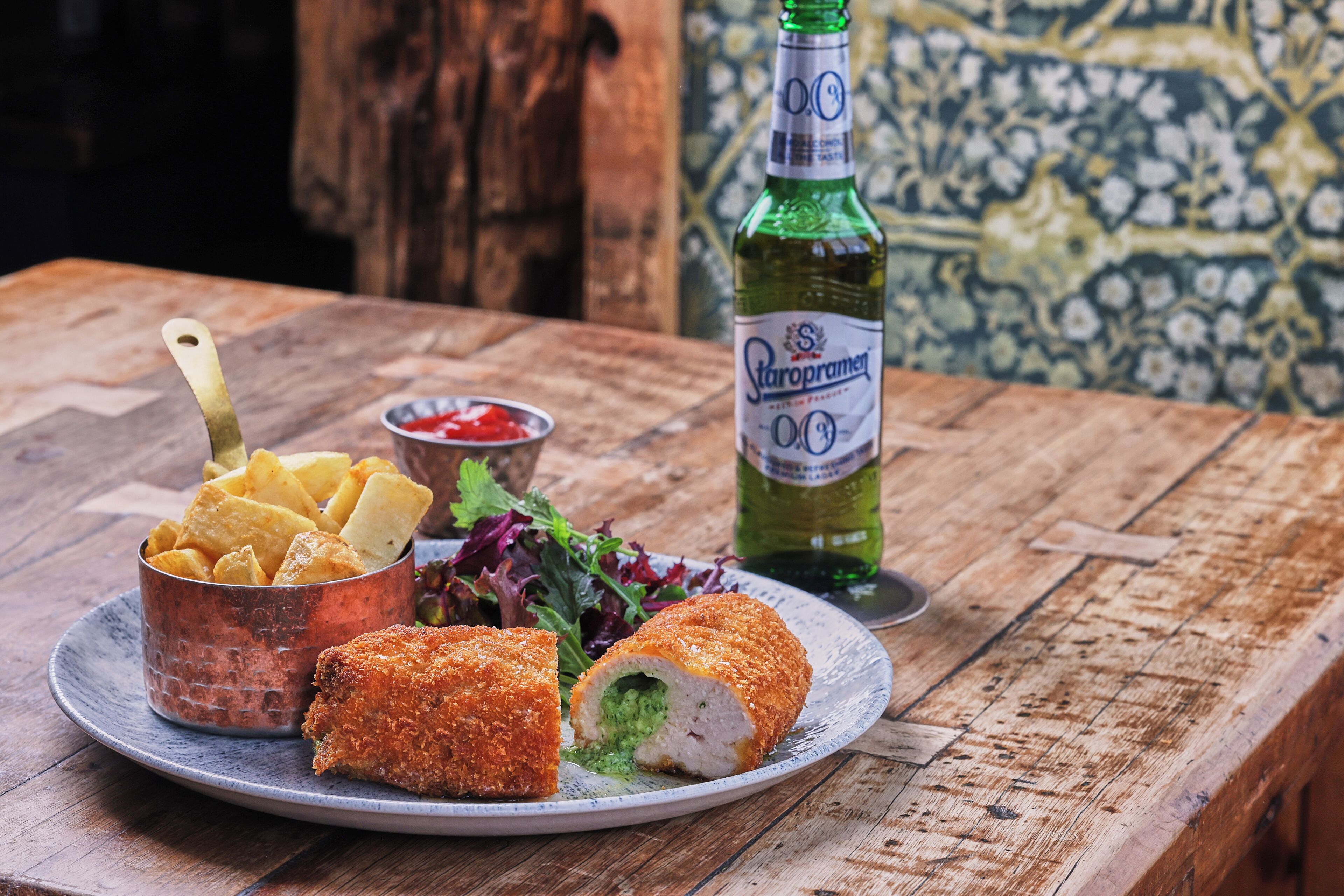 Une assiette remplie de plats frits, une bouteille et un bol de sauce, le tout posé sur une table en bois.