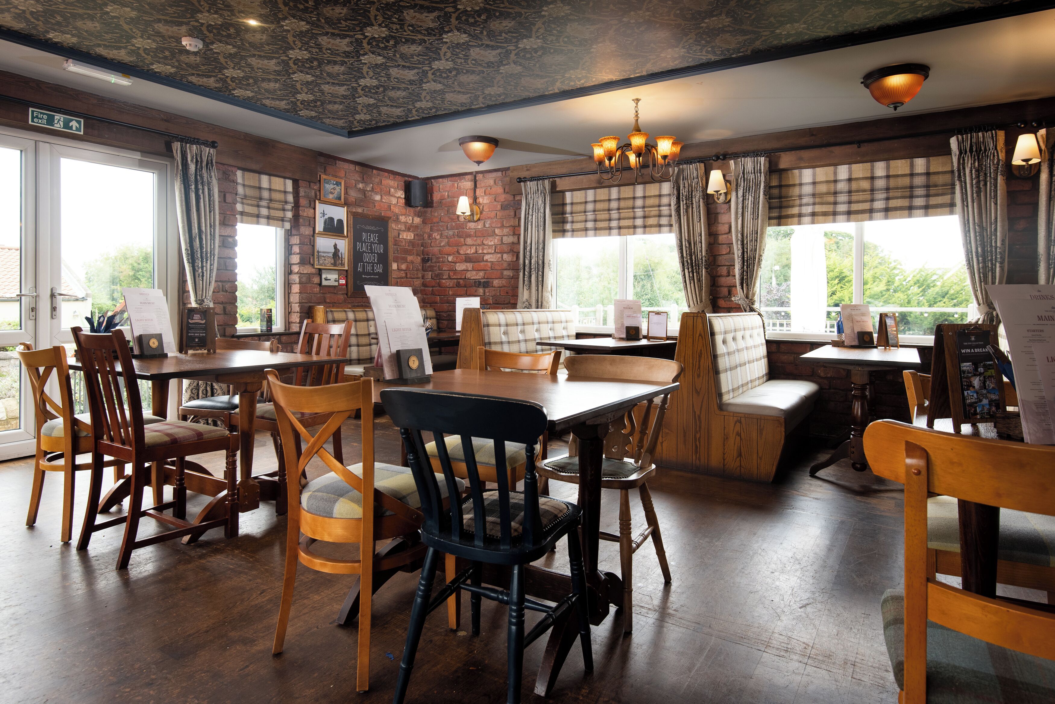 A restaurant with wooden furniture, brick walls, and large windows.