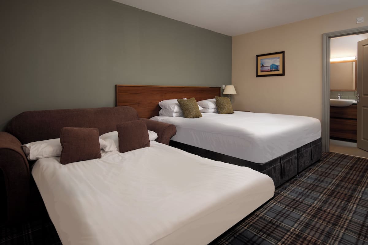 Une chambre d’hôtel avec deux lits, une tête de lit en bois, un tableau accroché au mur et une salle de bain visible à travers une porte ouverte.