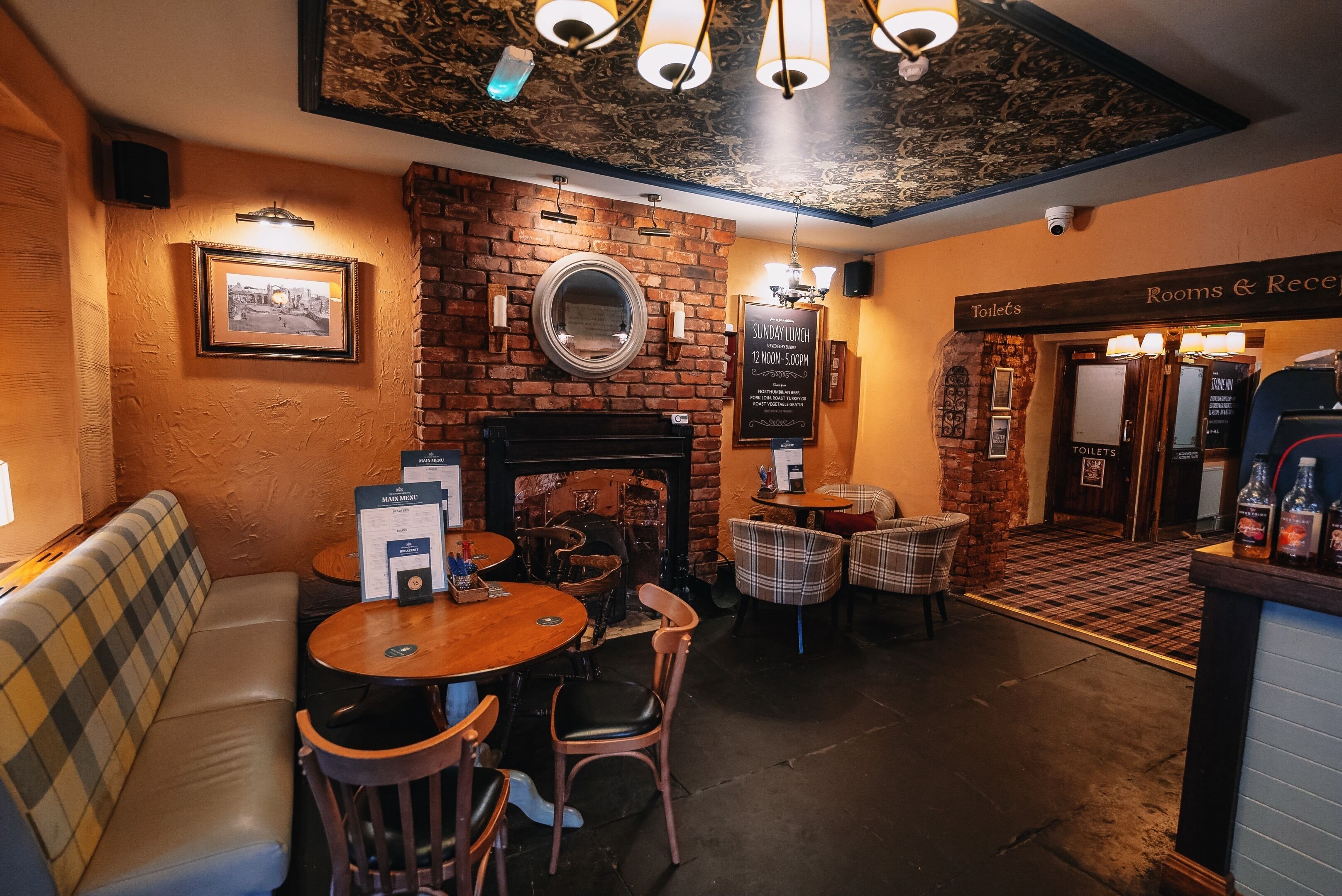 A cozy restaurant with a brick wall, a fireplace, and a seating area with tables and chairs.
