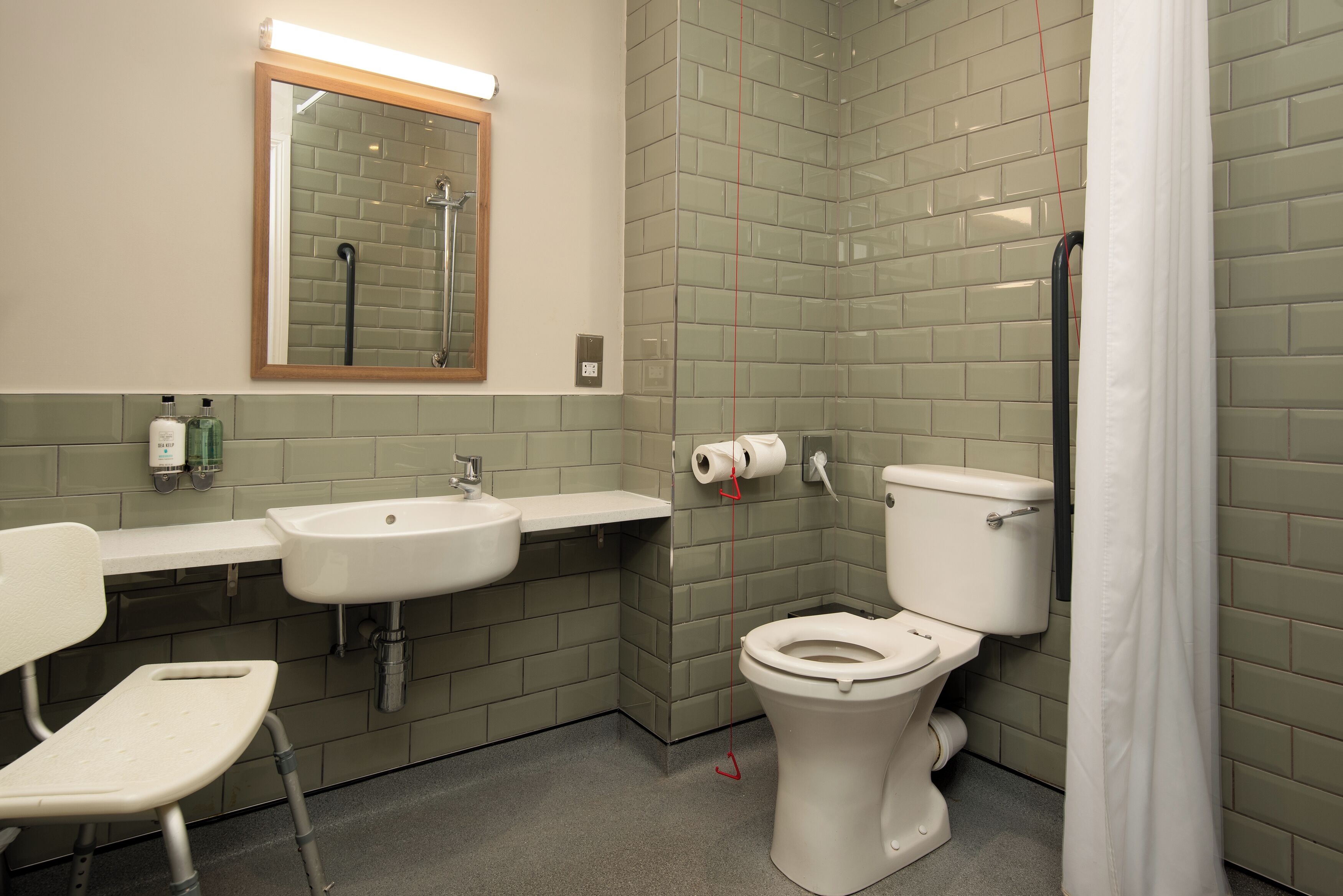 A bathroom with a sink, toilet, and shower. There is a mirror above the sink and a towel rack on the wall.