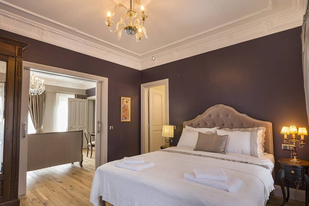 Une chambre spacieuse avec un grand lit, un lustre et une vue sur la salle de bain.