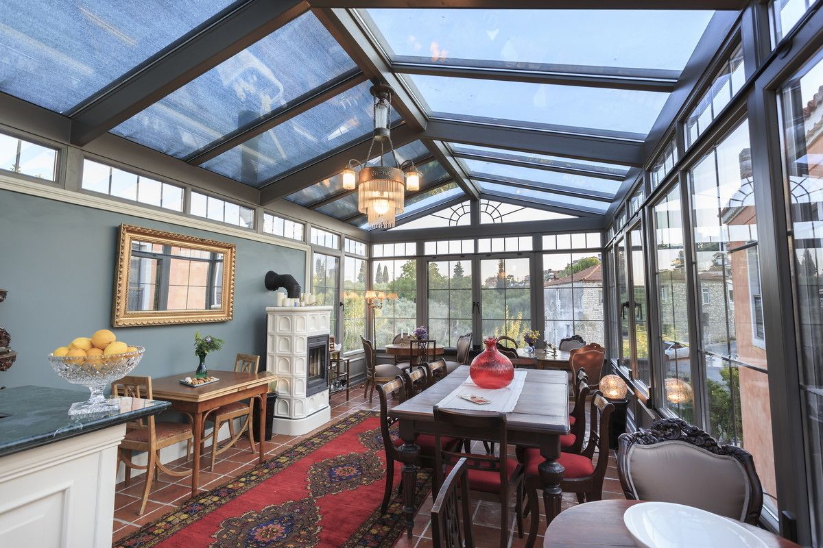 Un invernadero con techo de vidrio, chimenea y zona de comedor con sillas y mesa.