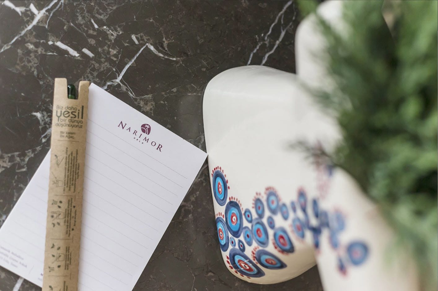 A notebook with 'NARIMOR' written on it, a pen, and a decorative mug with a blue and red pattern.