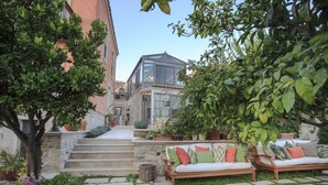 Un patio con escalones de piedra que conducen a una estructura con techo de vidrio, rodeado de plantas en macetas y mobiliario exterior.