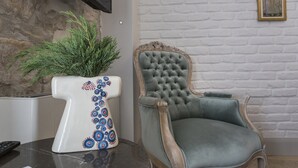 Una sala de estar moderna con una pared de acento de piedra, un jarrón blanco decorativo con motivos azules y rojos, y un sillón clásico tapizado en gris.