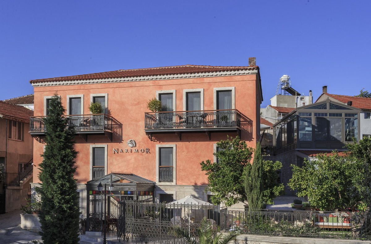 A building with the name "NARIMOR" on the facade, featuring balconies and a small covered area with tables and chairs.