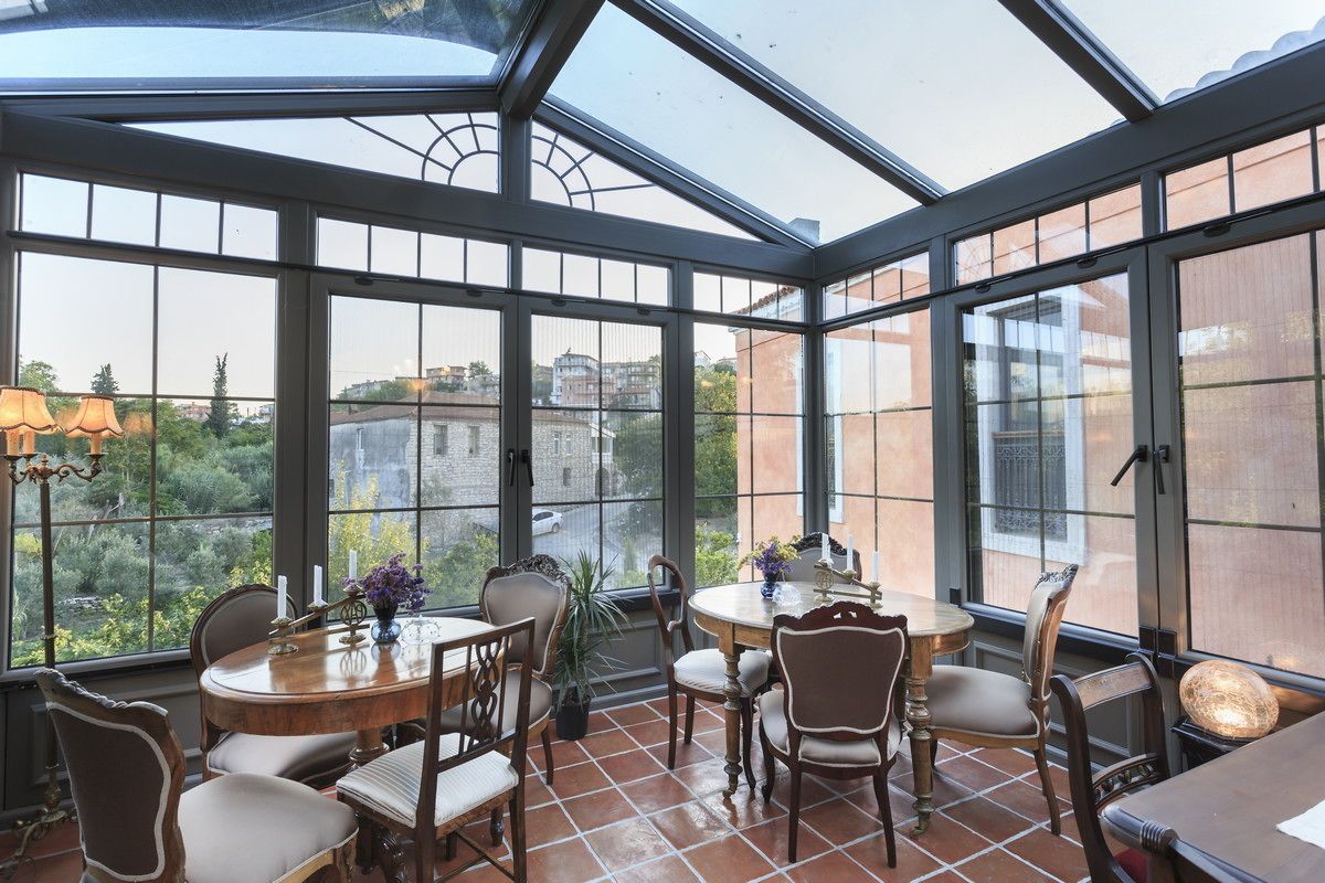 A sunroom with large windows, a dining table, chairs, and a potted plant.