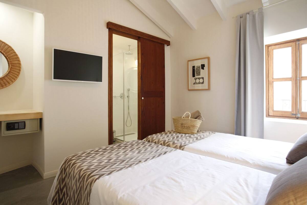 Une chambre d’hôtel avec deux lits, une douche, une télévision, un tableau encadré et une fenêtre avec des rideaux.