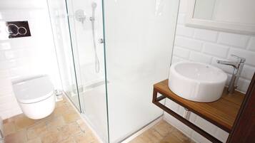 Un baño moderno con cabina de ducha de vidrio, inodoro y lavamanos con estante de madera.