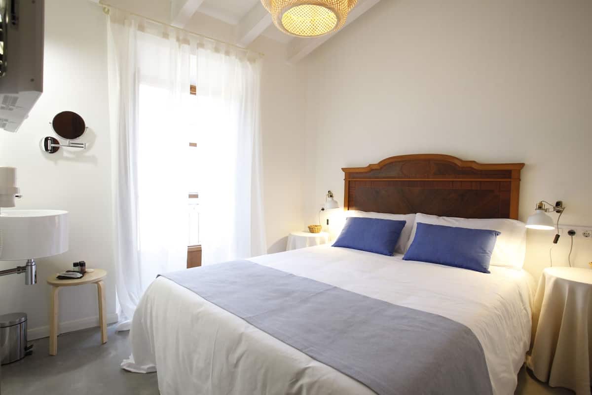 Une chambre à coucher bien rangée, avec un grand lit, des tables de chevet, un miroir et un luminaire suspendu.