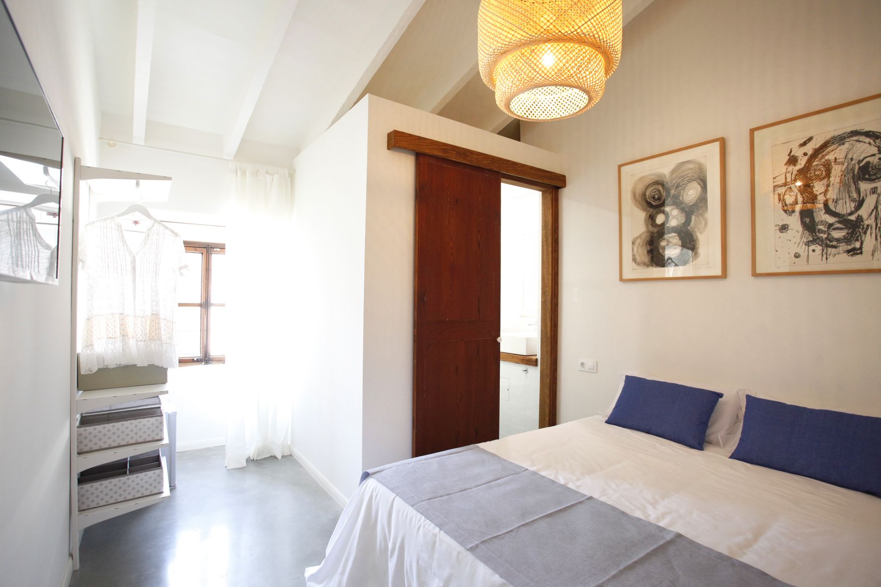 A bedroom with a bed, a wooden door, and two framed artworks on the wall.