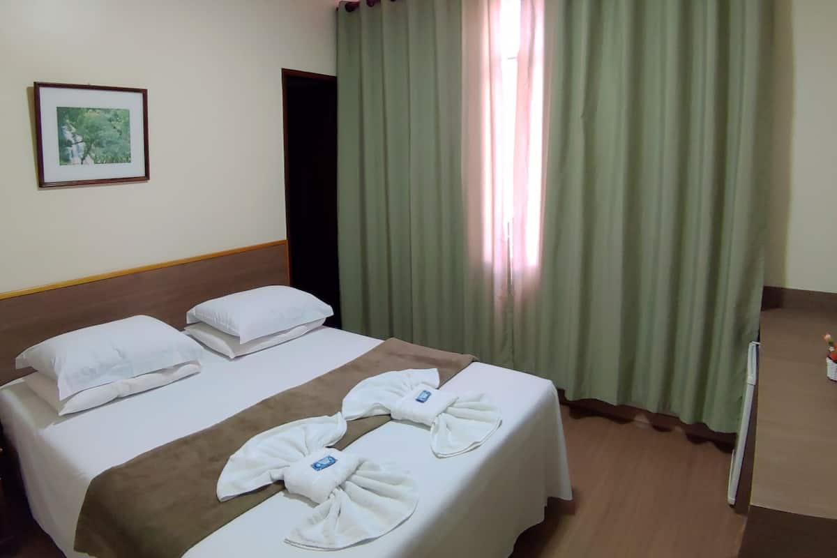 Ein Hotelzimmer mit einem Bett, Kissen, einem Nachttisch, einem gerahmten Bild und grünen Vorhängen.
