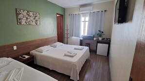 Une chambre d’hôtel avec deux lits, un petit bureau, une plante et un téléviseur.