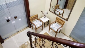 Un escalier avec une rampe en bois, une petite table sur laquelle est posé un vase de fleurs, et deux chaises en bois avec des coussins à motifs.