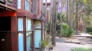 A wooden building with large windows and a stone pathway leading to a wooden deck. - Altos Medanos - Cabañas y Club de Bosque (Mar de Las Pampas)