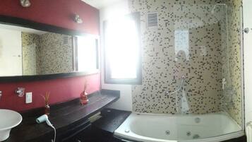 Une salle de bain avec un lavabo blanc, un miroir, une douche dont le mur est recouvert de mosaïques, et une fenêtre laissant entrer la lumière naturelle.