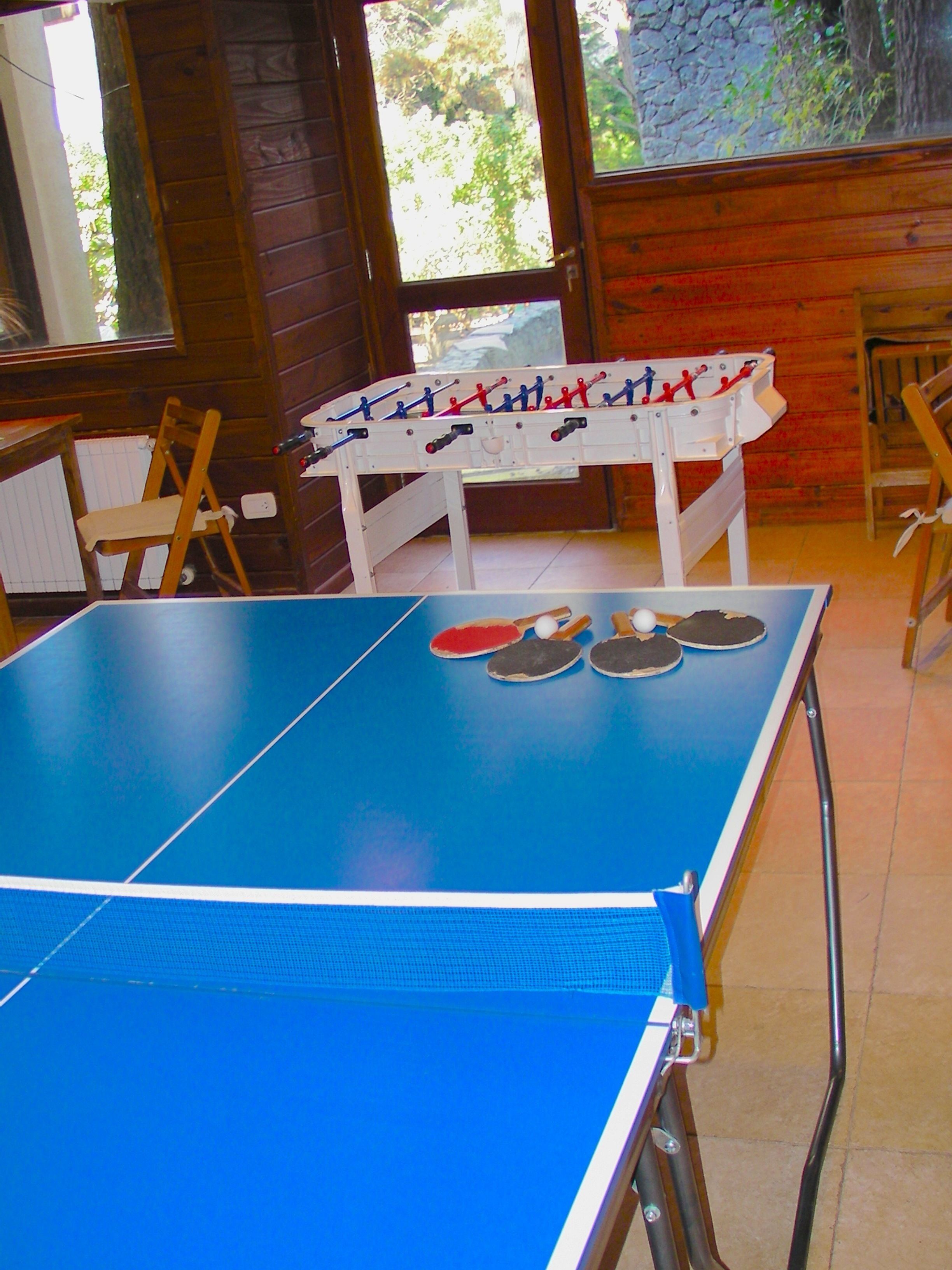 A ping pong table with paddles and balls, a wooden chair, and a table with a cloth.