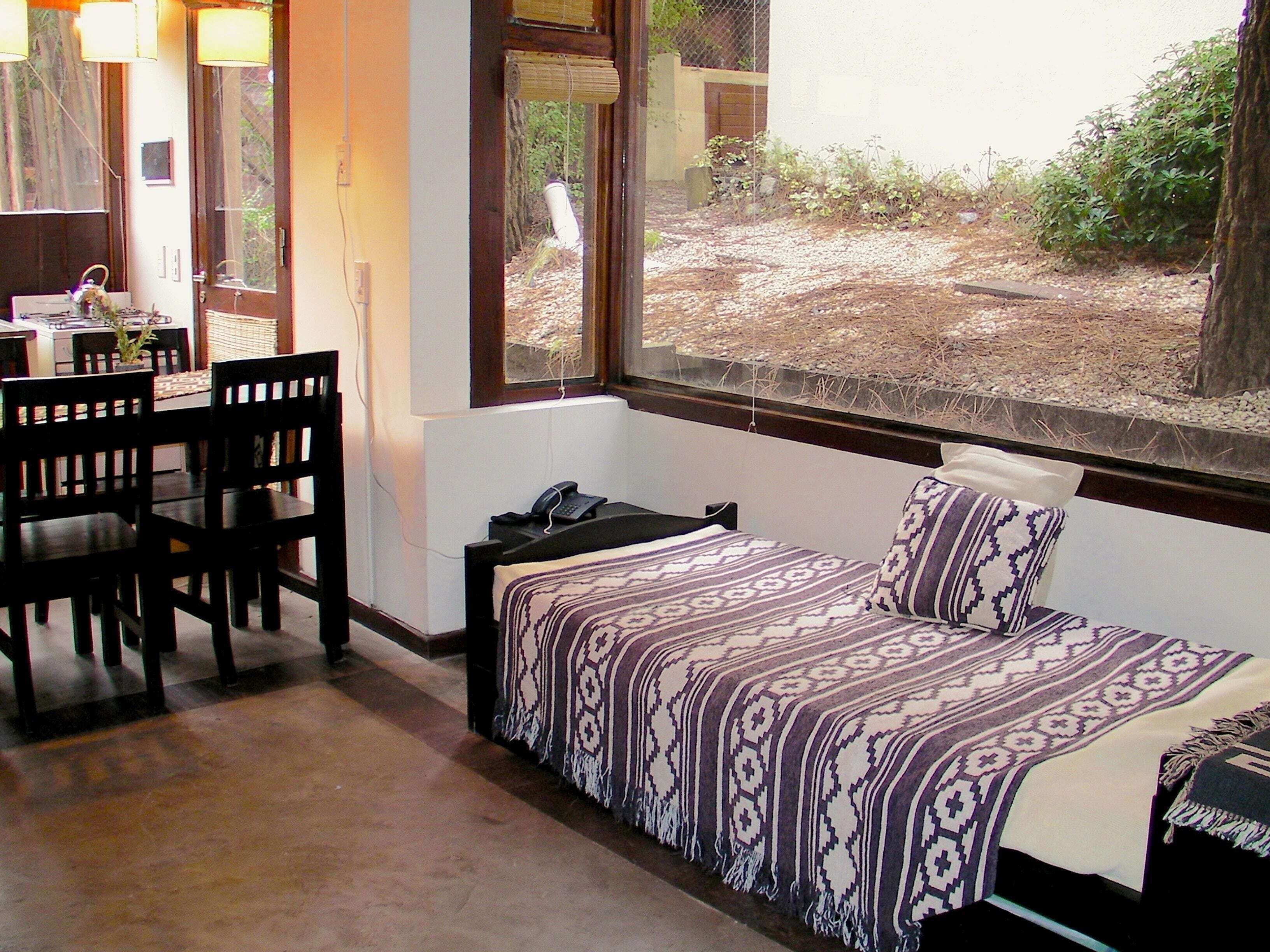 Habitación con cama, escritorio y sillas. Se ve el exterior a través de la ventana.