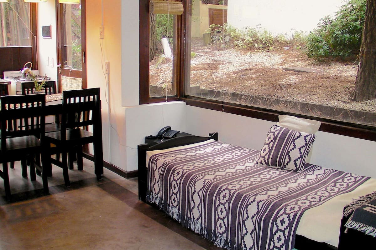 A room with a bed, a desk, and chairs. There is a window with a view of the outdoors.