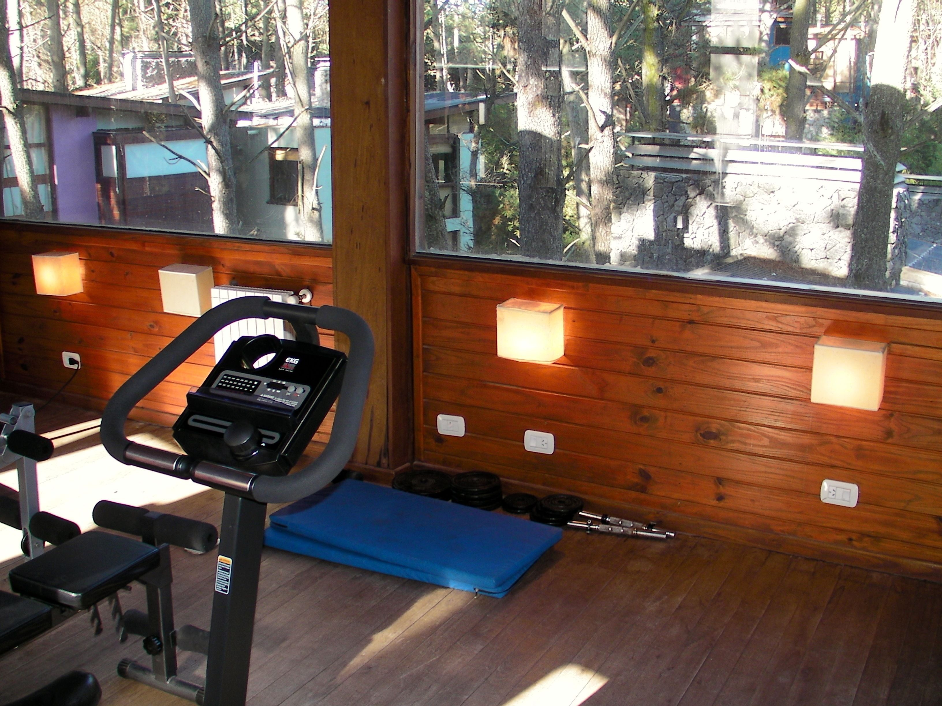 Un gimnasio con equipo de ejercicio, una colchoneta azul y una ventana que ofrece vistas a árboles y edificios.