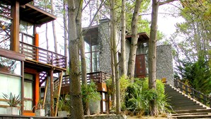 A modern building with a stone facade, wooden deck, and a staircase leading to an upper level. - Altos Medanos - Cabañas y Club de Bosque (Mar de Las Pampas)