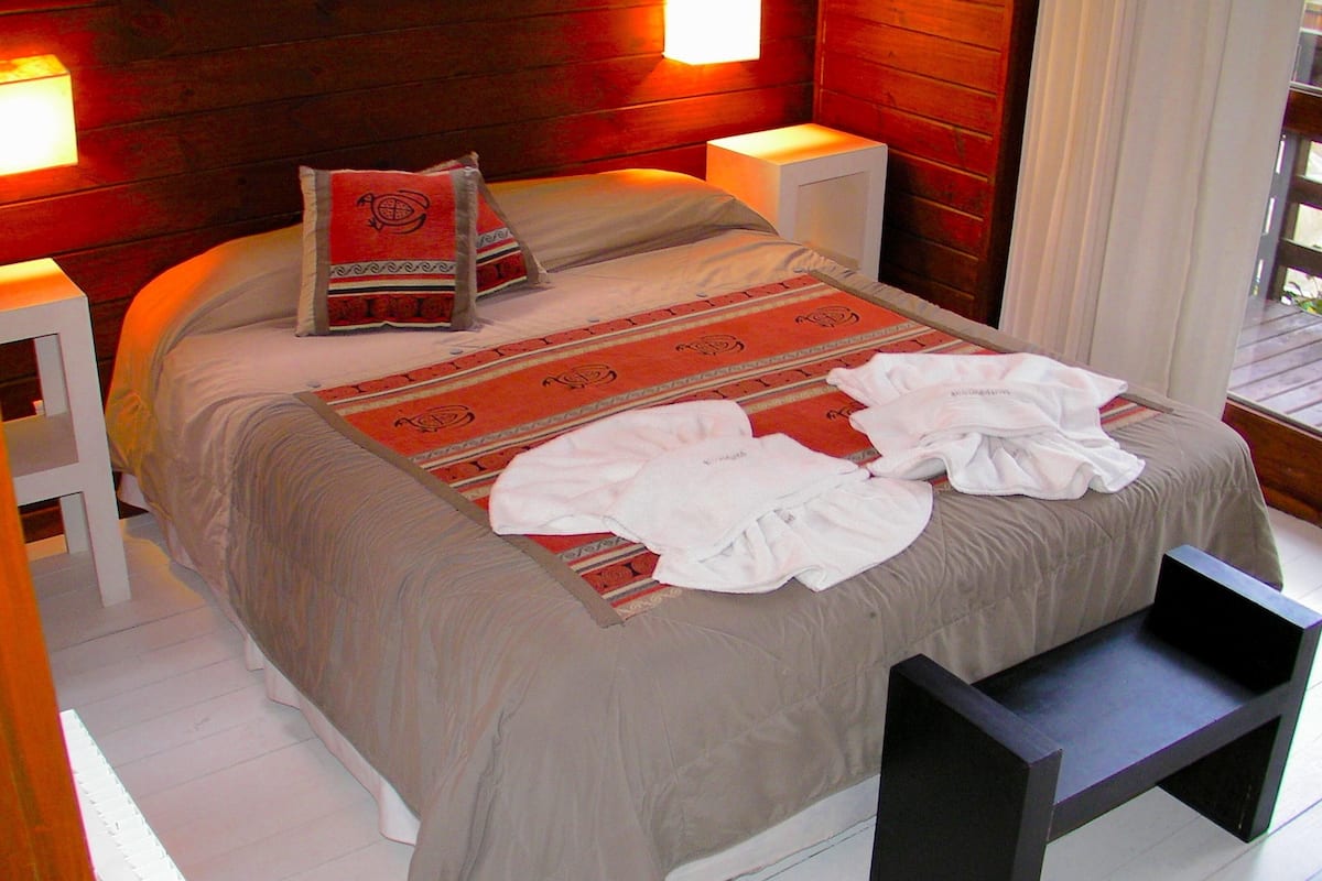 A neatly made bed with a patterned bedspread, pillows, and a bedside table with a lamp.