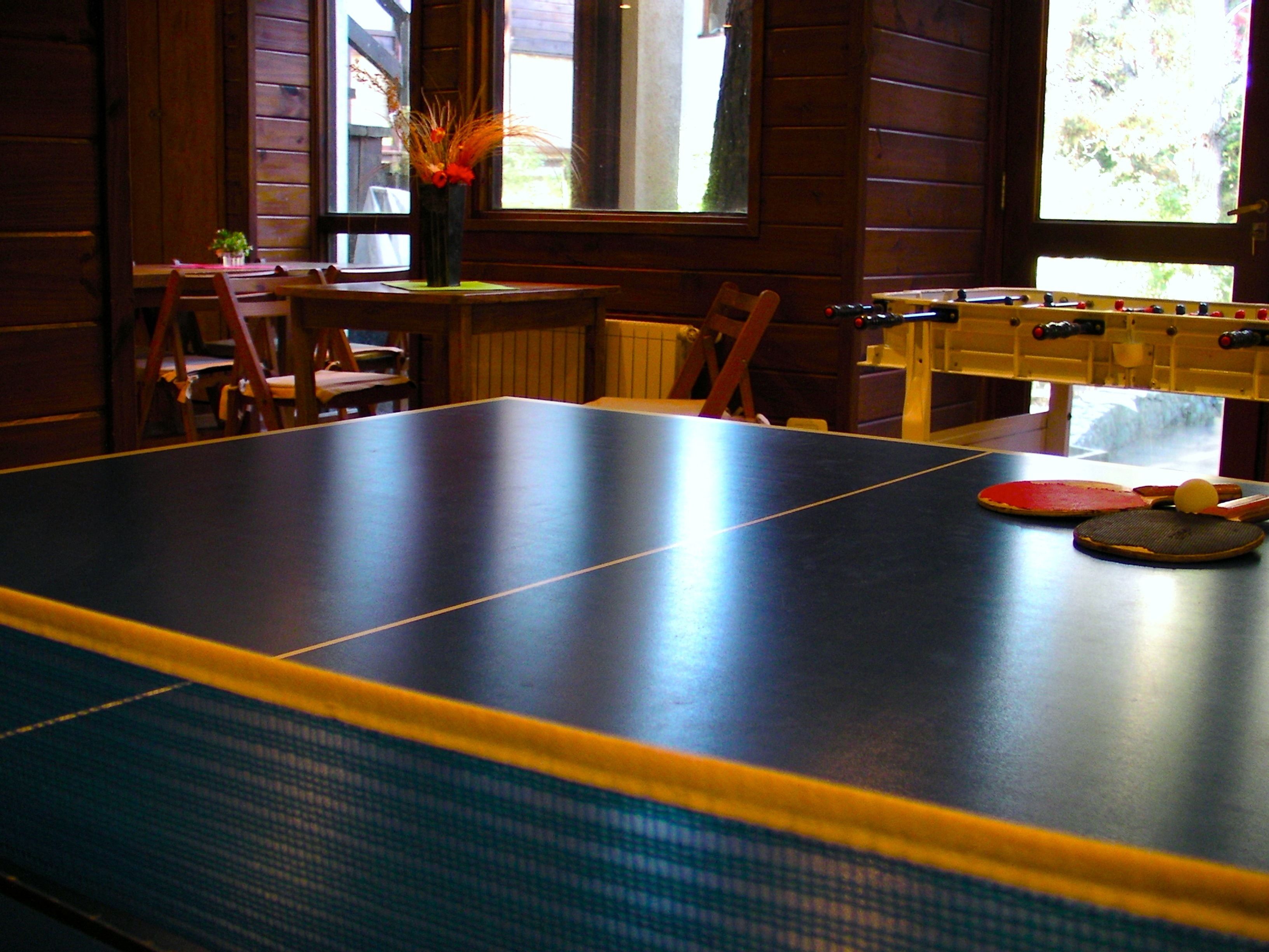 A ping pong table with a foosball table beside it, wooden walls, and a window with a view.