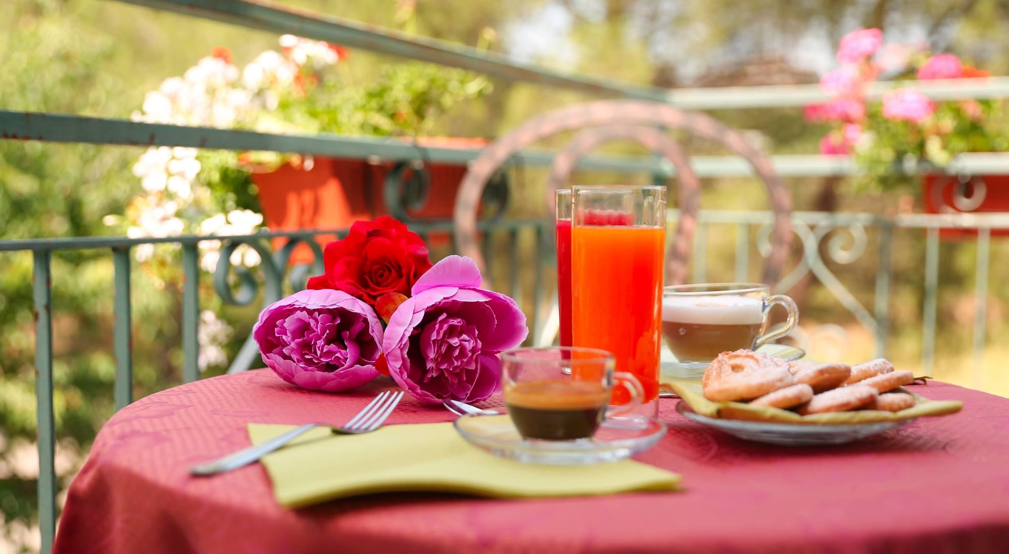 Una mesa cubierta con mantel rojo, un vaso de jugo de naranja, una taza de café, pasteles y flores.