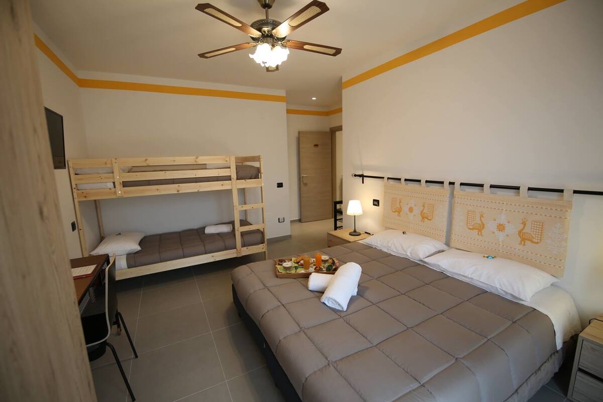 A bedroom with a bunk bed, a single bed, a desk, and a ceiling fan.