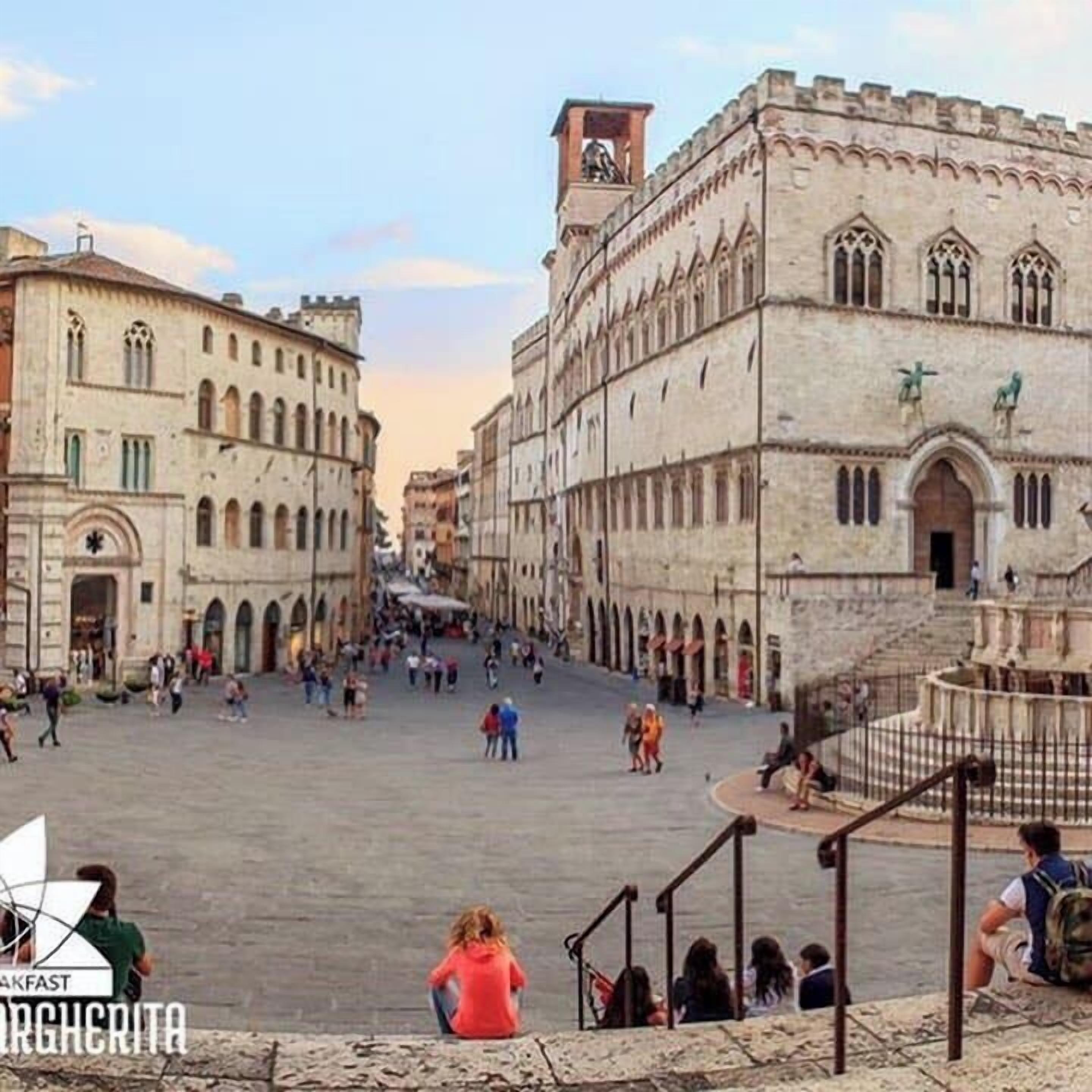 A historic square with buildings featuring arched windows and a central fountain.