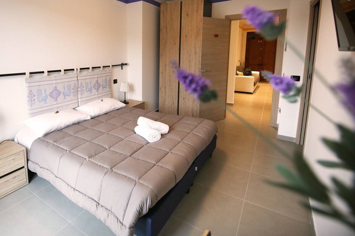 A modern bedroom with a large bed, a wooden headboard, and a nightstand.