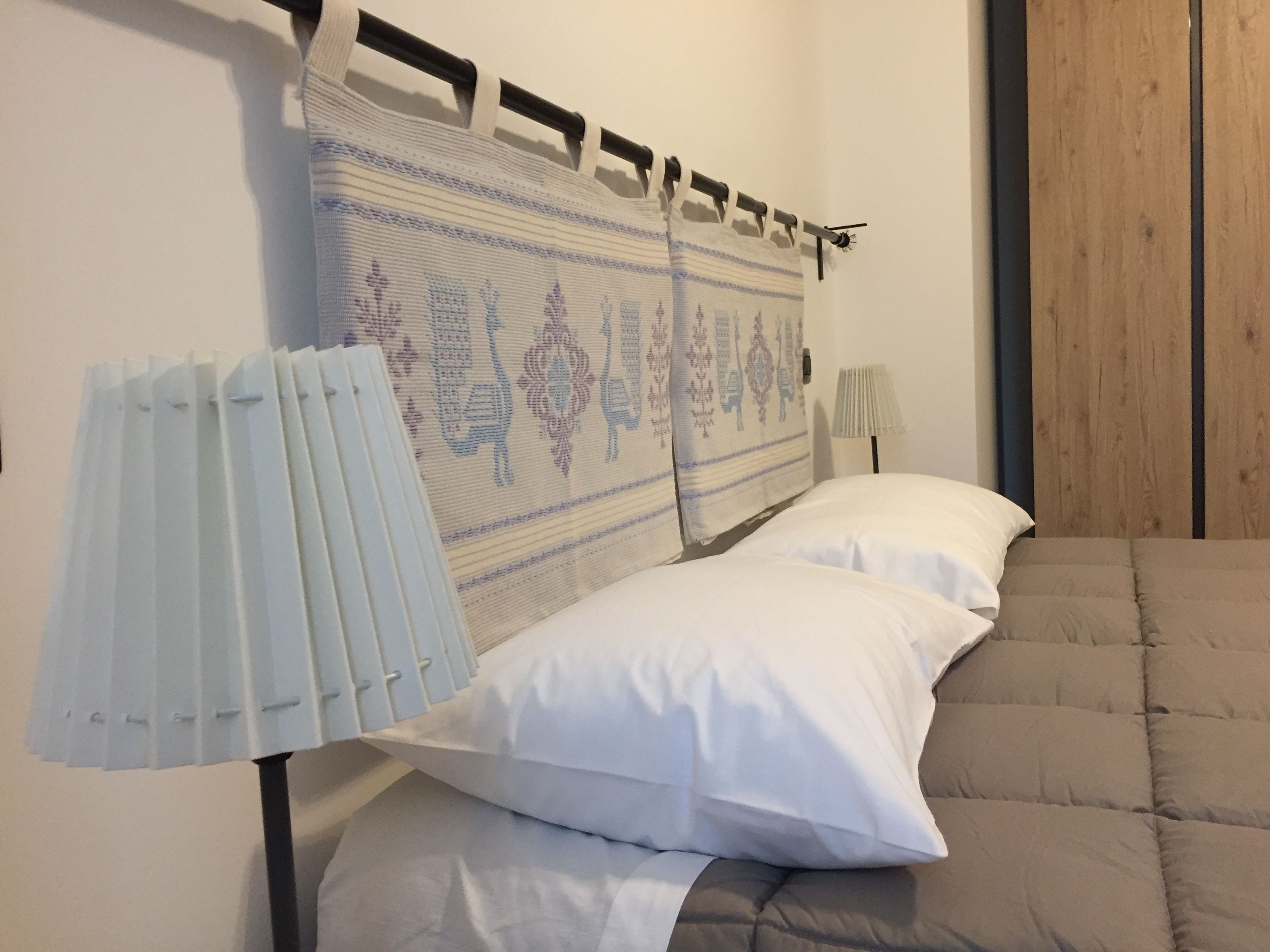 Een slaapkamer met een bed, witte kussens, een hoofdbord met een patroon en een bedlampje.