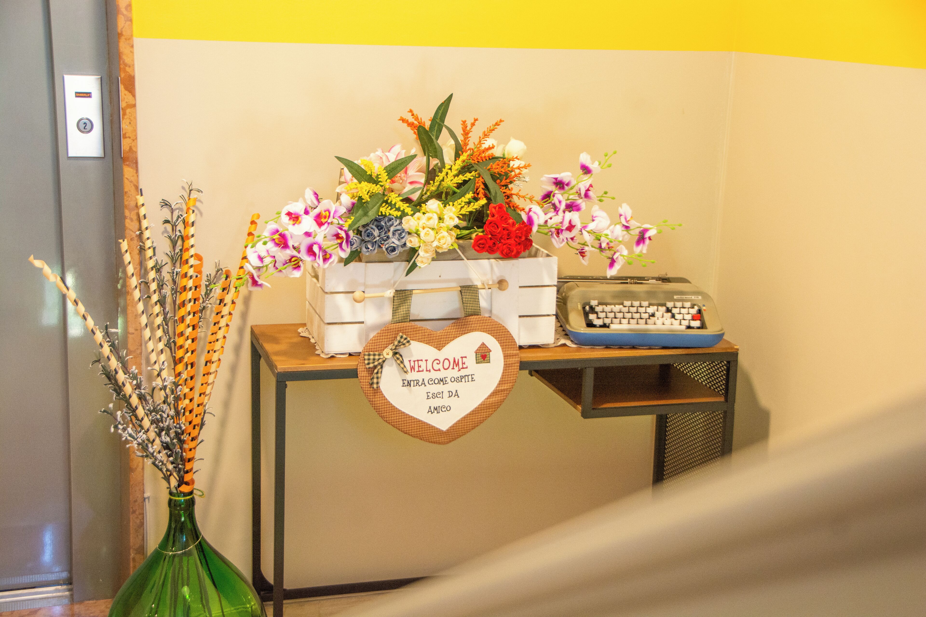 A reception desk with a welcome sign, a vase with dried flowers, and a vintage typewriter.