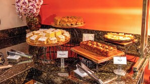 Um buffet com diversos doces à mostra, incluindo bolos e uma composição de frutas.