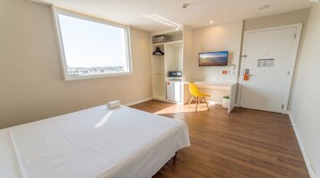 Una camera d'albergo con un letto, una scrivania, una sedia, un armadio, una televisione e una finestra con vista.