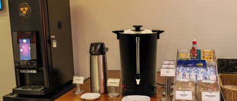 Una estación de café con una máquina de café, dispensador de agua caliente, una jarra de café y diferentes opciones de cápsulas.