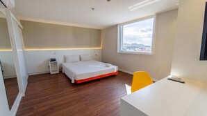 Quarto de hotel moderno com cama, mesa de cabeceira, cadeira e vista da cidade.