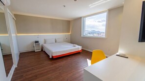 Quarto de hotel moderno com cama, mesa de cabeceira, cadeira e vista da cidade.